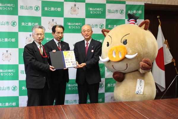 まるいのの横で、市長と男性2名が一緒に切手が入ったファイルを持っている写真